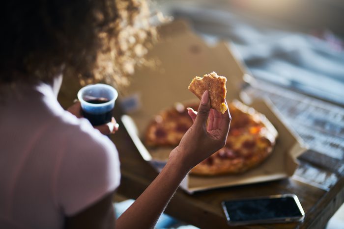 woman eating pizza and drinking cola while sitting on sofa