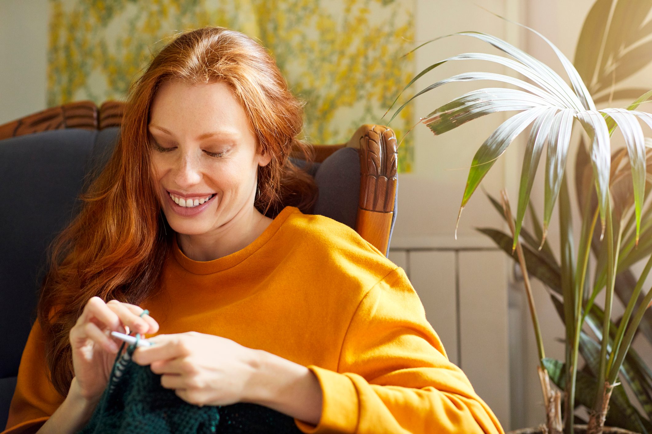 Woman knitting while sitting by plant on chair