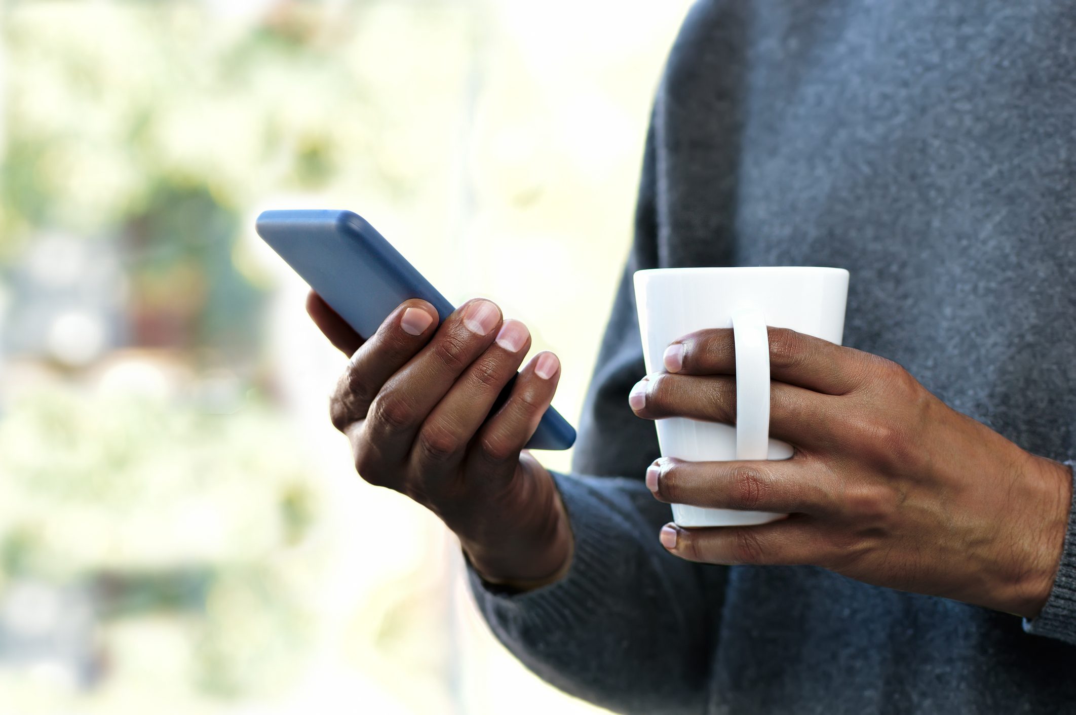 close up of person holding coffee mug and smartphone