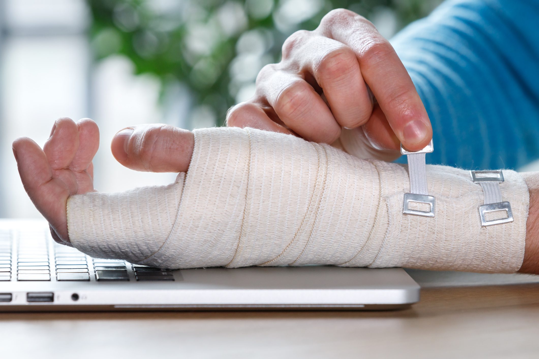 Close up of man arms wrapping his painful wrist with Flexible elastic supportive orthopedic bandage caused by prolonged work on laptop. Carpal tunnel syndrome, arthritis, arm sprain concept.