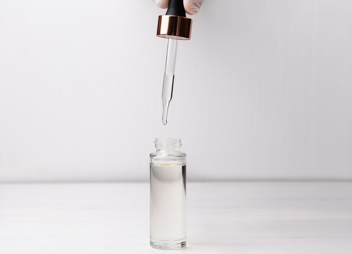 Hand in medical gloves holding dropper and bottle of beauty serum. Beauty product for skincare concept.