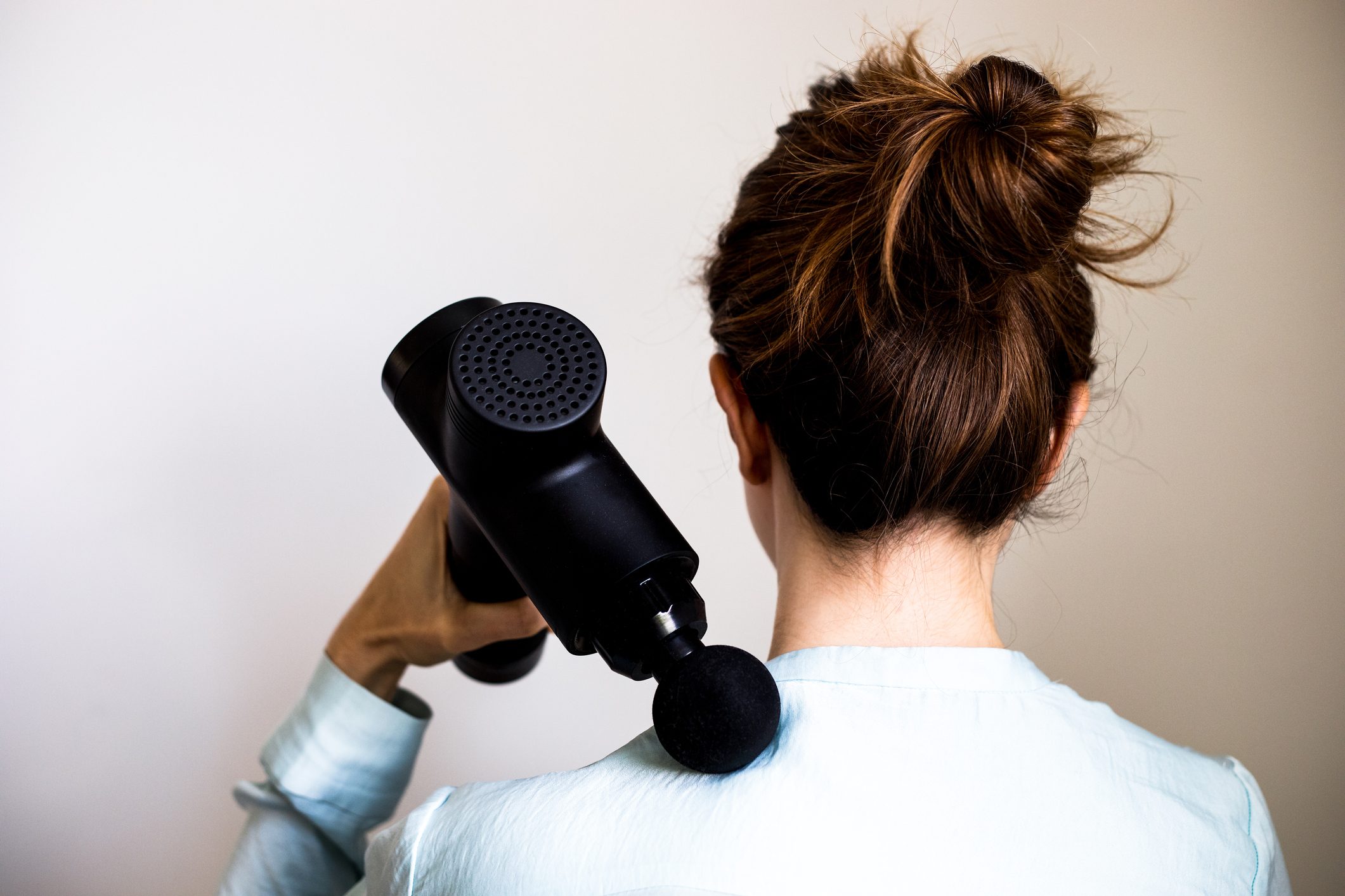 Rear view of a woman using massage gun / machine