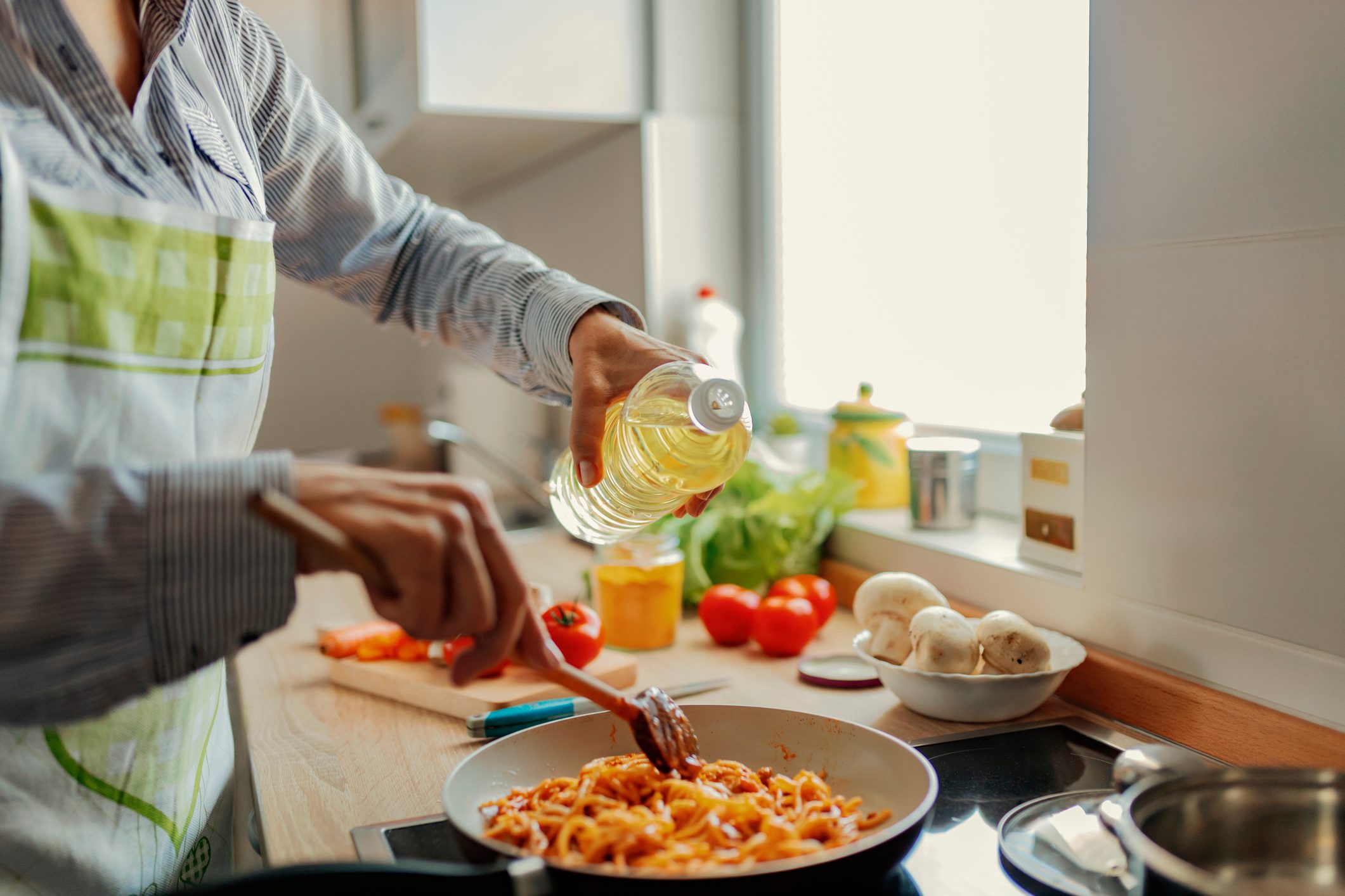 Woman adding oil from bottle into pan