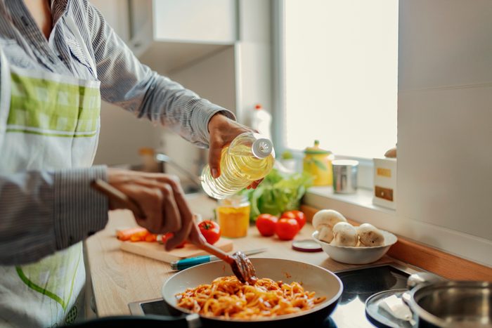 Woman adding oil from bottle into pan