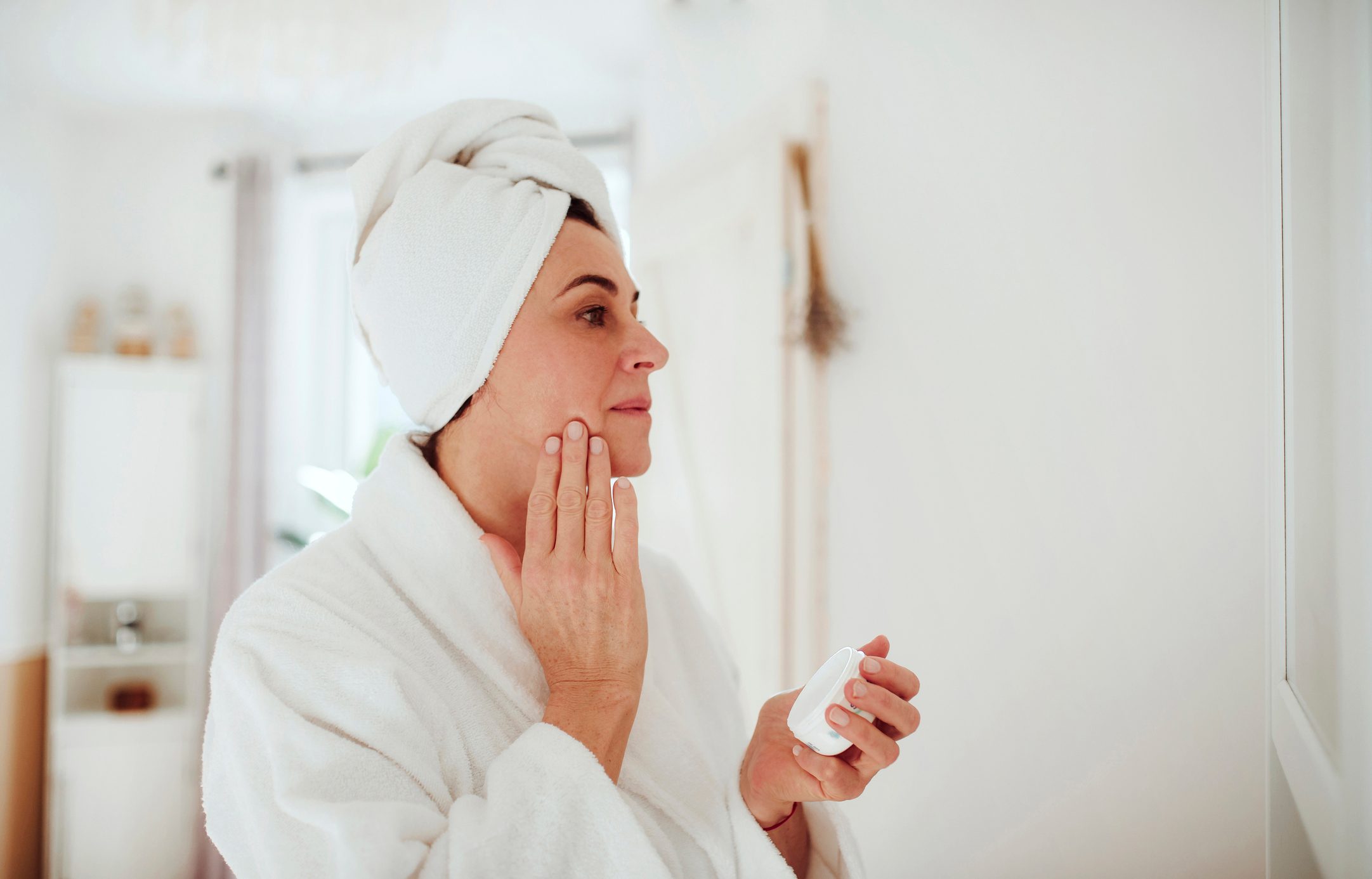 Mature woman in a bathroom at home applying moisturizer