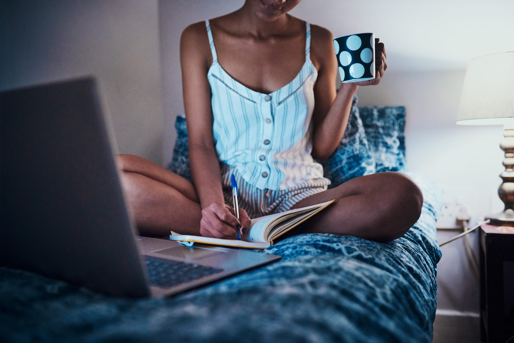 woman writes in journal with cup of coffee and laptop