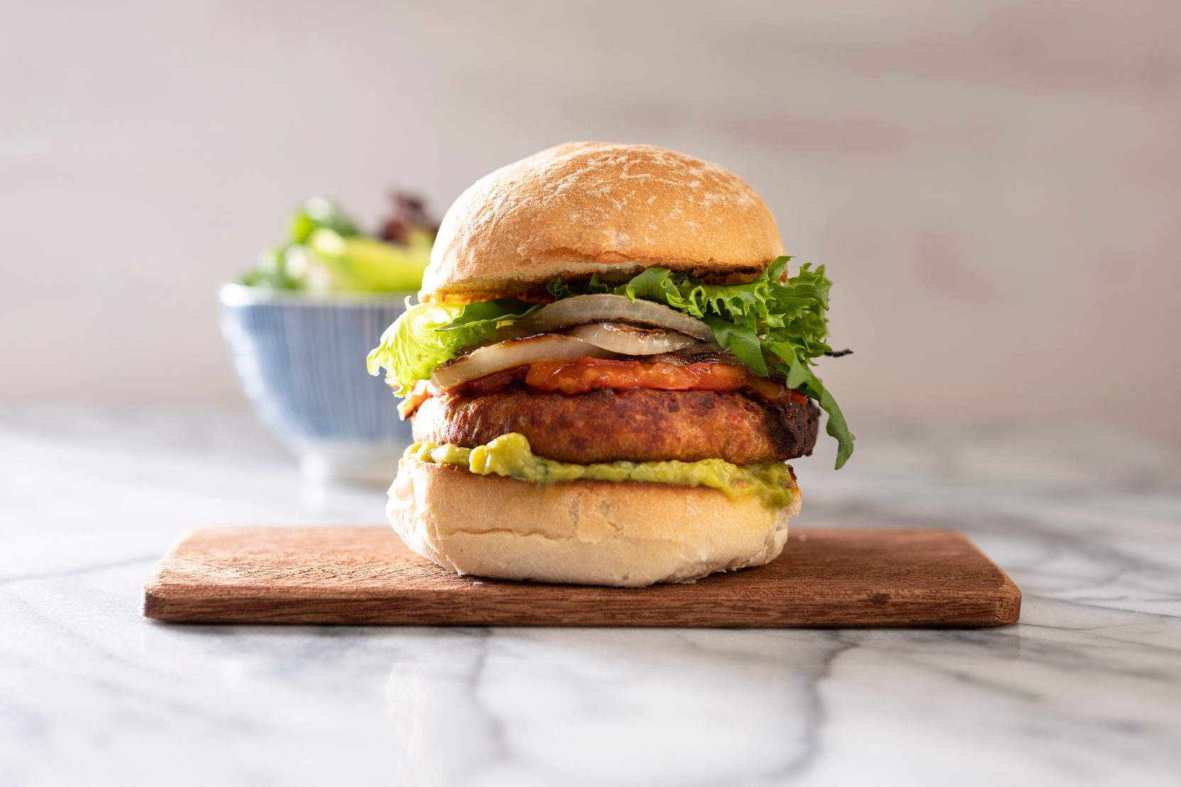 Vegan burger on a chopping board. Bowl of salad in the background.