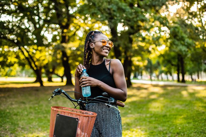 woman drinking water outside with a bike
