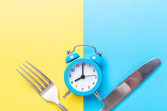 Blue alarm clock, fork, knife on colored paper background. Intermittent fasting concept