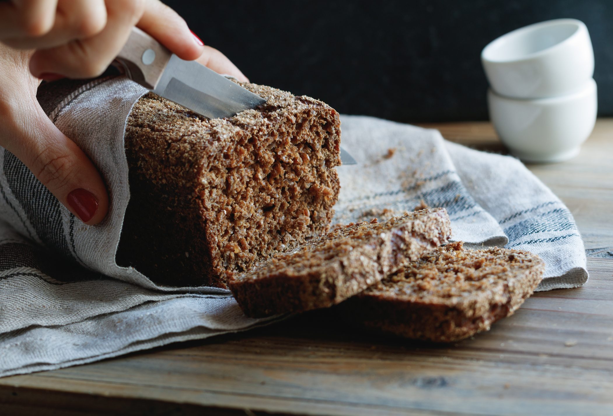 The girl cuts whole-wheat rye bread on a wooden table.
