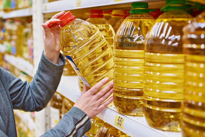 woman taking large bottle of oil off of shelf at grocery store