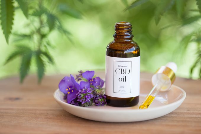 CBD Cannabis Oil (cannabidiol) bottle and dropper on small plate atop wooden surface.
