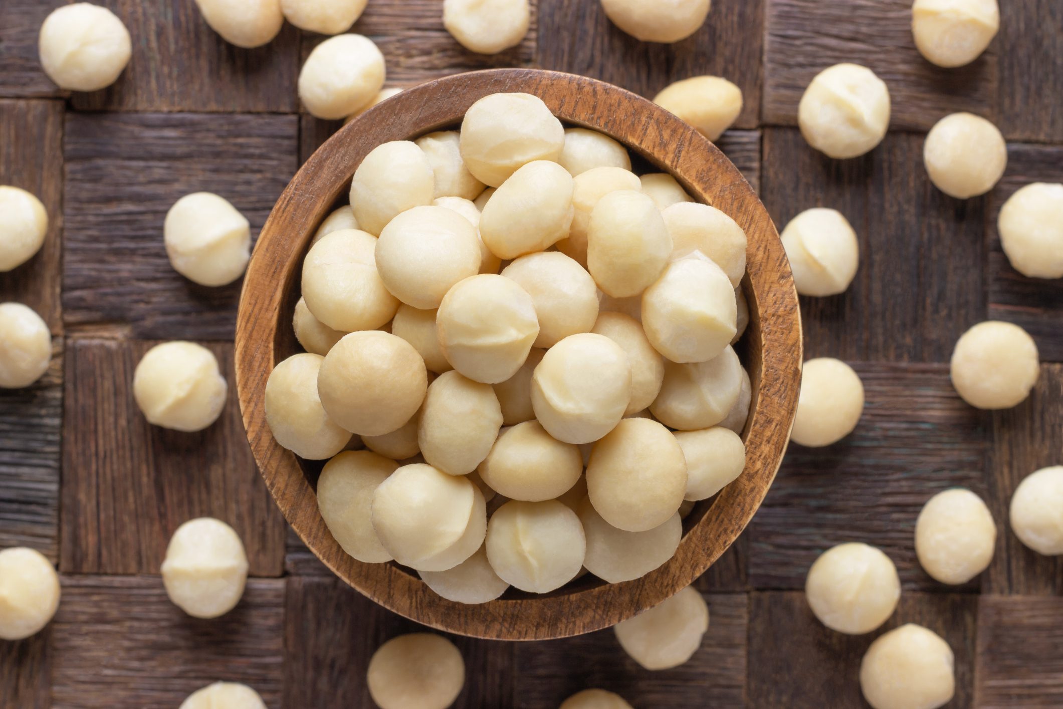 macadamia nuts peeled in wooden bowl, top view.