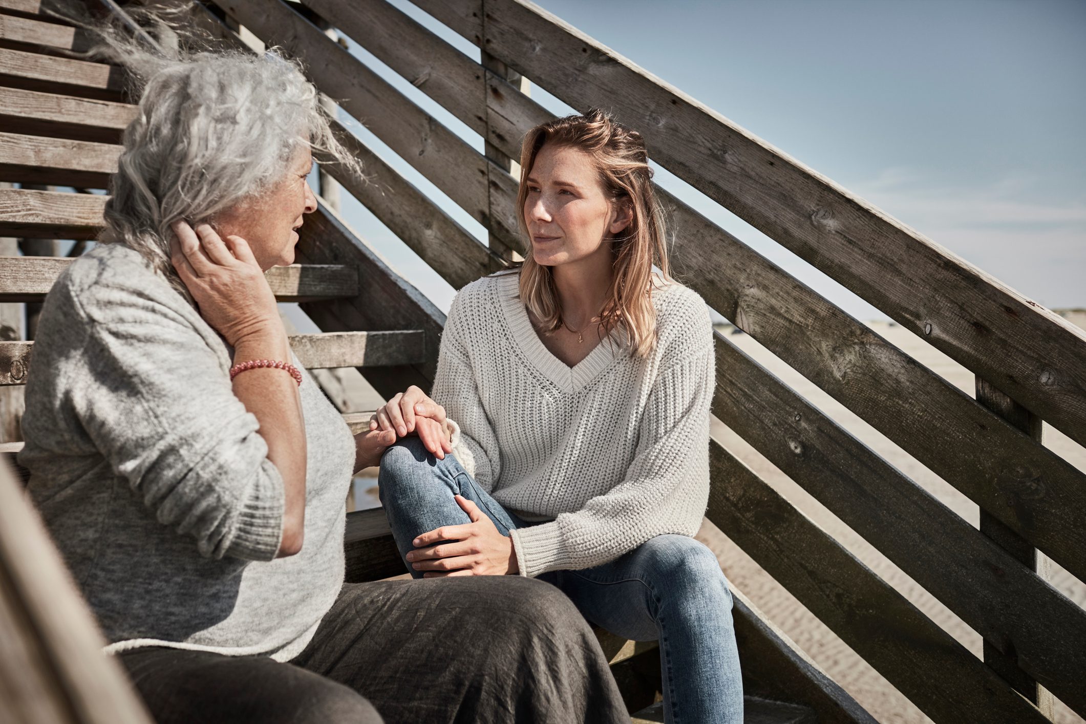 Senior woman talking with adult daughter on footbridge at the beach