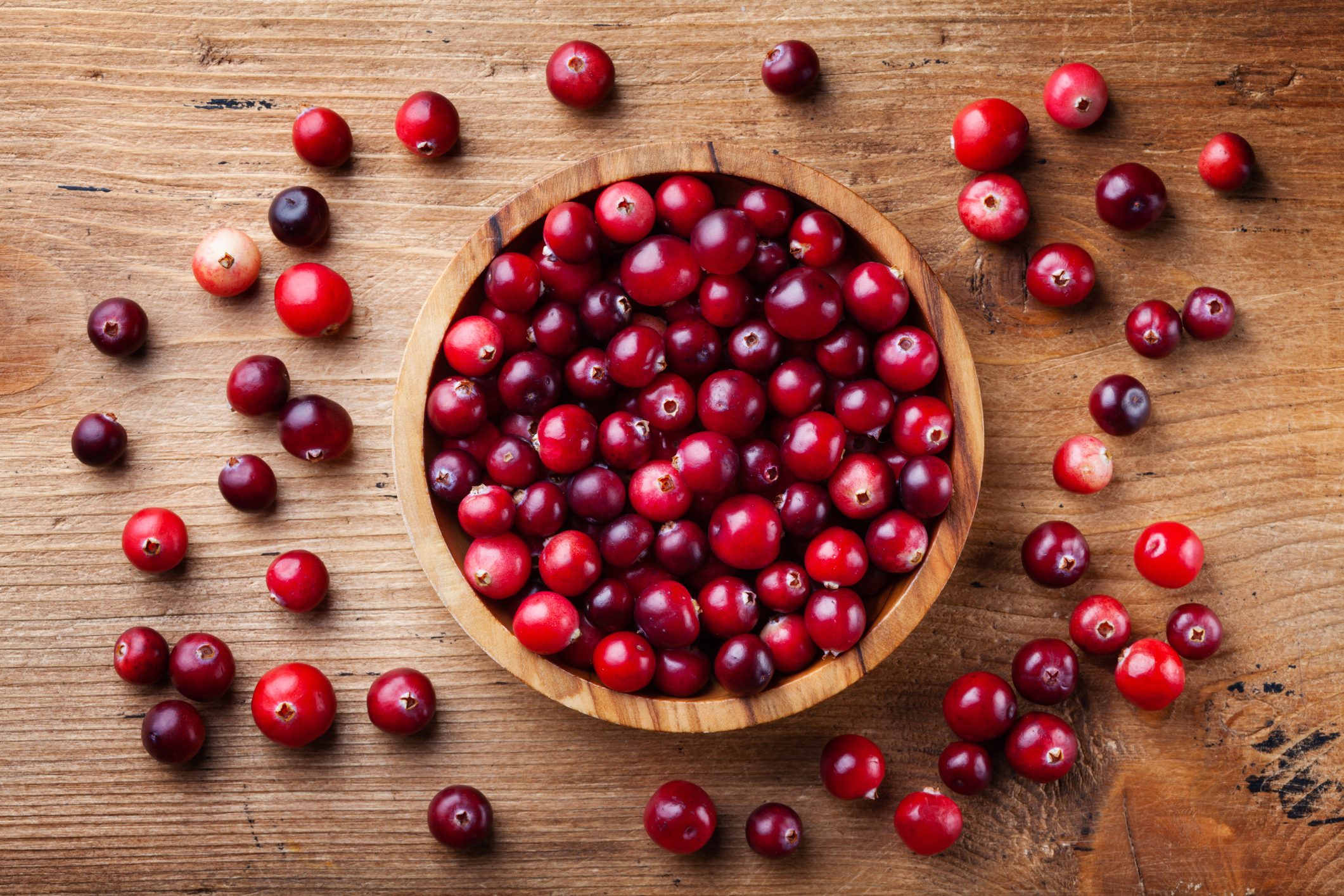 Fresh raw cranberry in wooden bowl on rustic table top view.