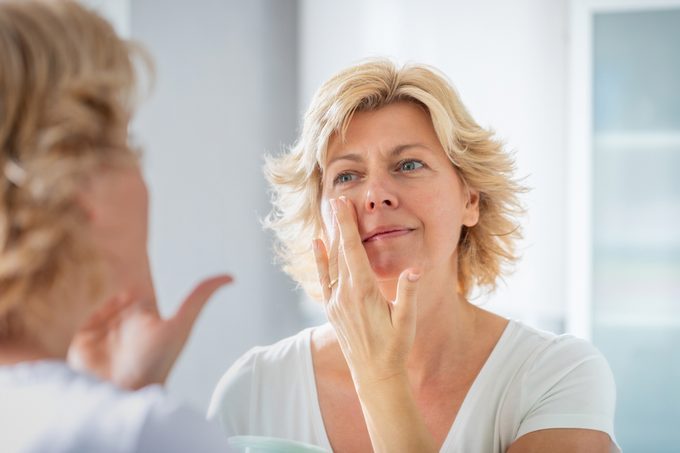 Mid adult woman spreading a layer of facial cream in front of the mirror