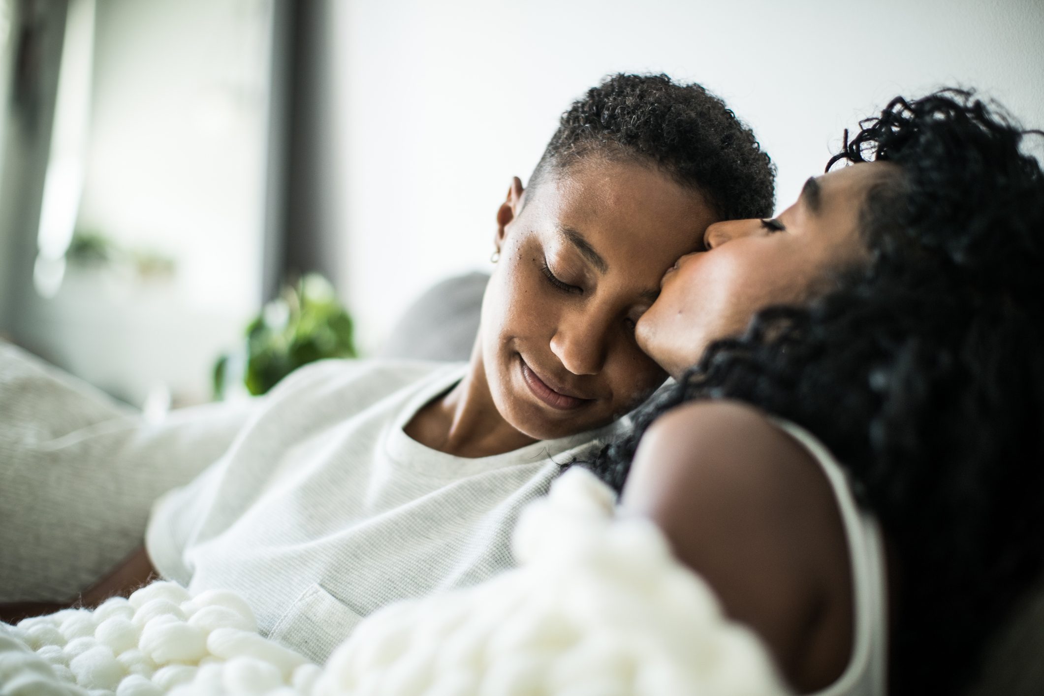 Lesbian couple at home snuggling under blanket