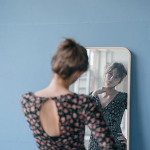 Young woman in vintage dress looking into mirror