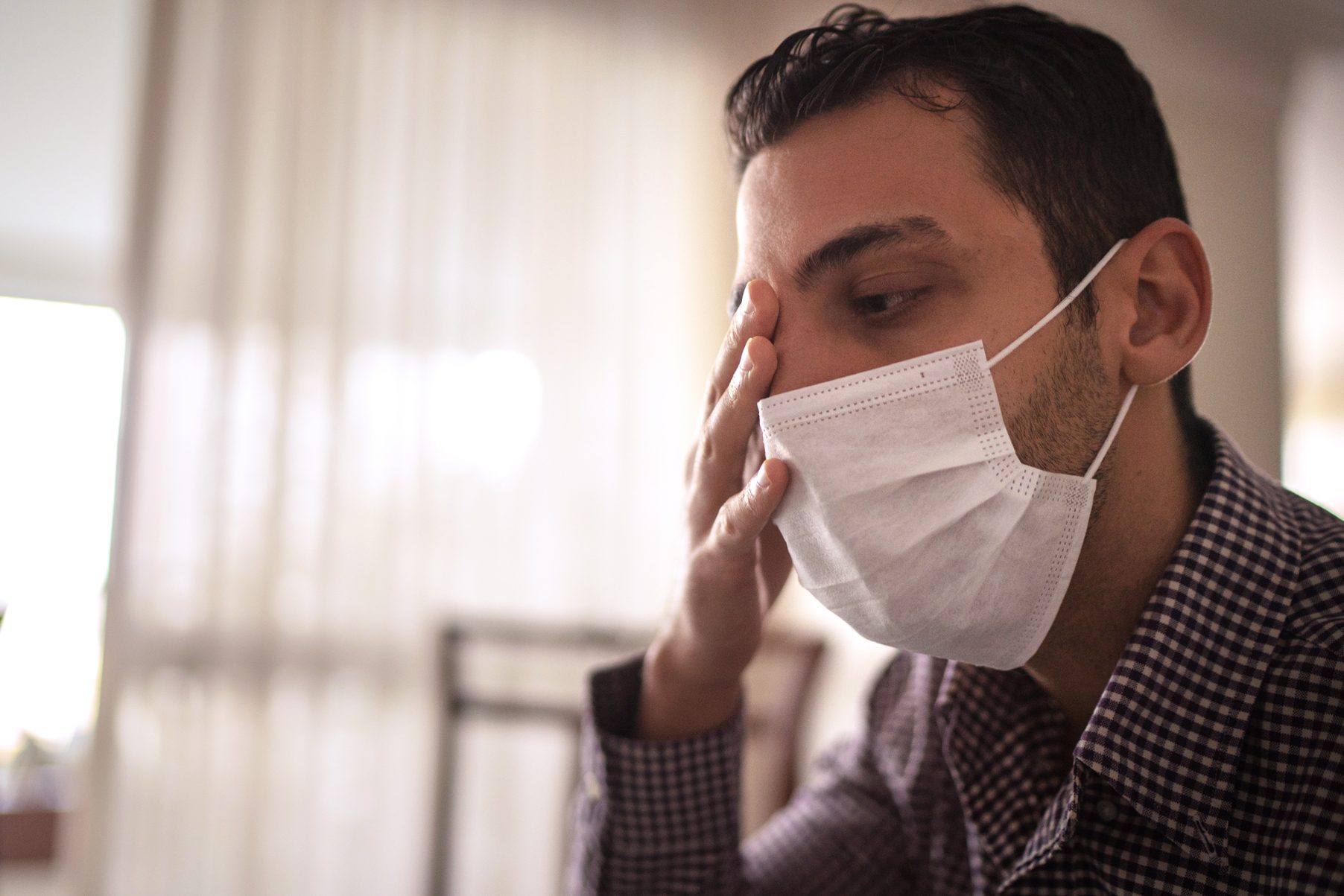 man wearing face mask and touching eye