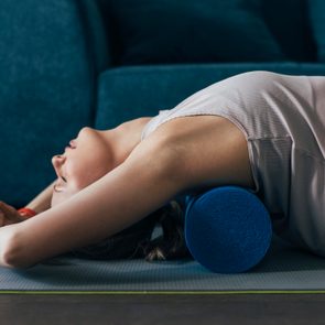 Working Out at Home Woman is Sportswear Using a Roller to Massage Back Muscles