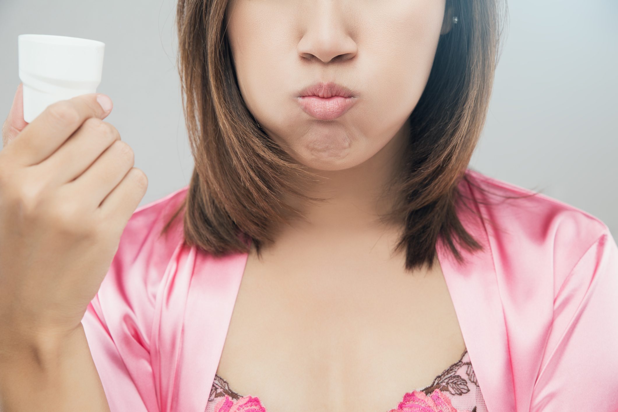 Midsection Of Young Woman Gargling Against Gray Background