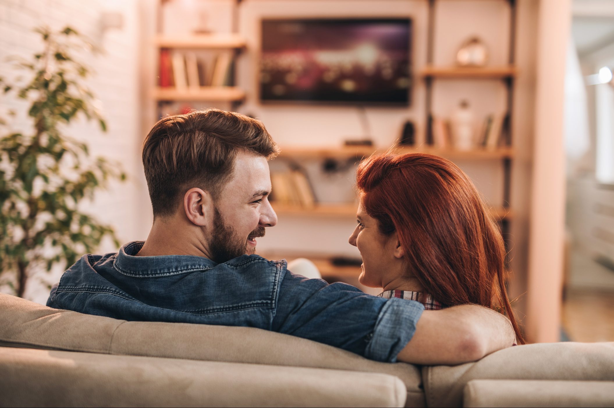 Back view of happy couple talking while watching TV at home.