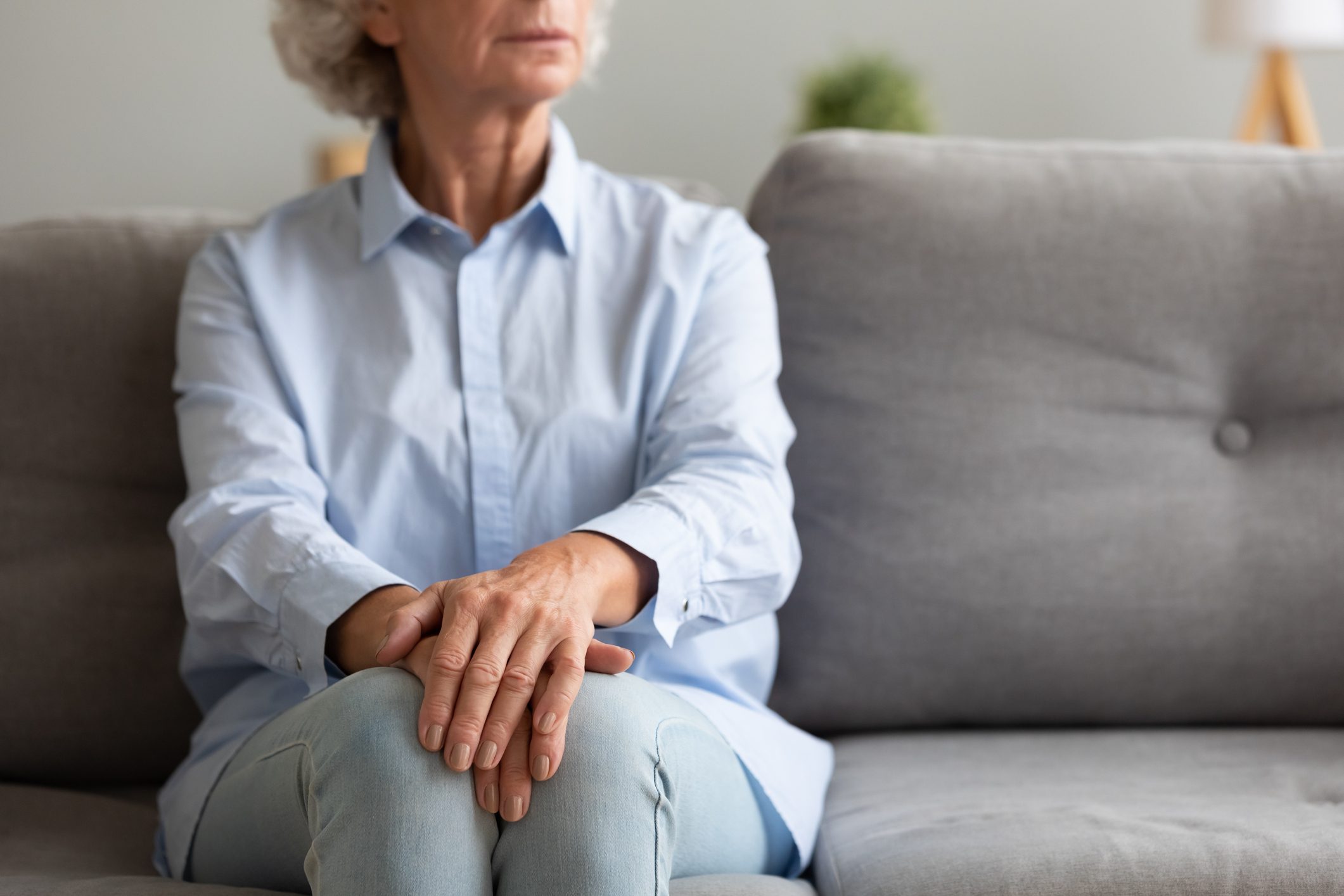 Unhappy depressed senior woman sit alone on sofa, closeup view