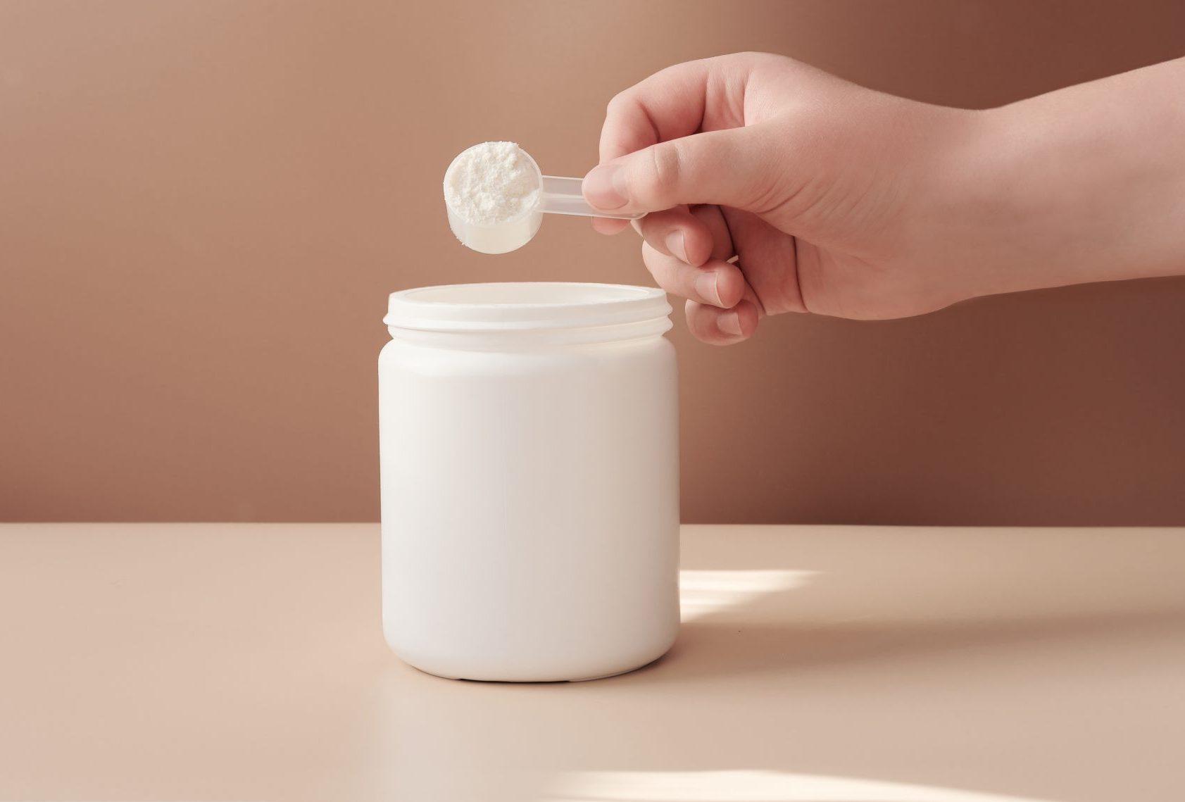 hand with scoop of powder from jar