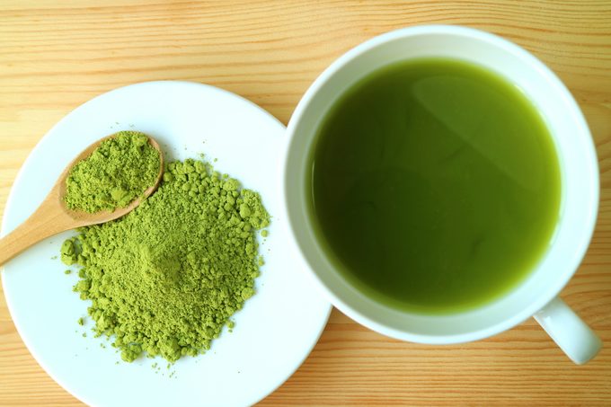 Cup of Hot Matcha Green Tea with a Plate of Matcha Tea Powder on Wooden Table