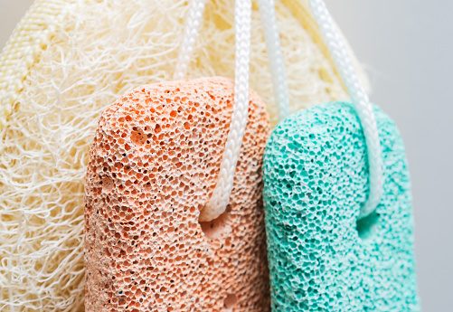 Orange and green pumice stones and wisp of bast or bath sponge on the wall. Close-up, selective focus.