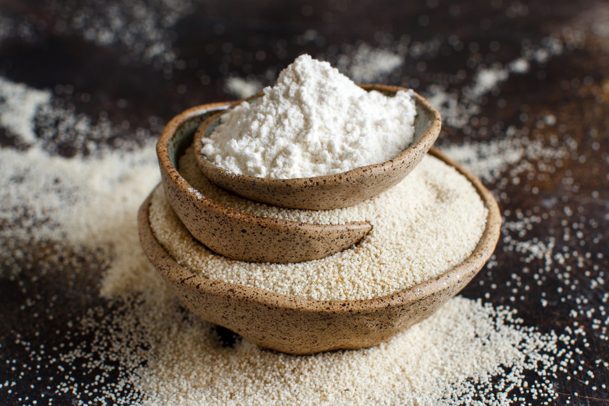 Raw fonio flour and seeds in bowls on dark background