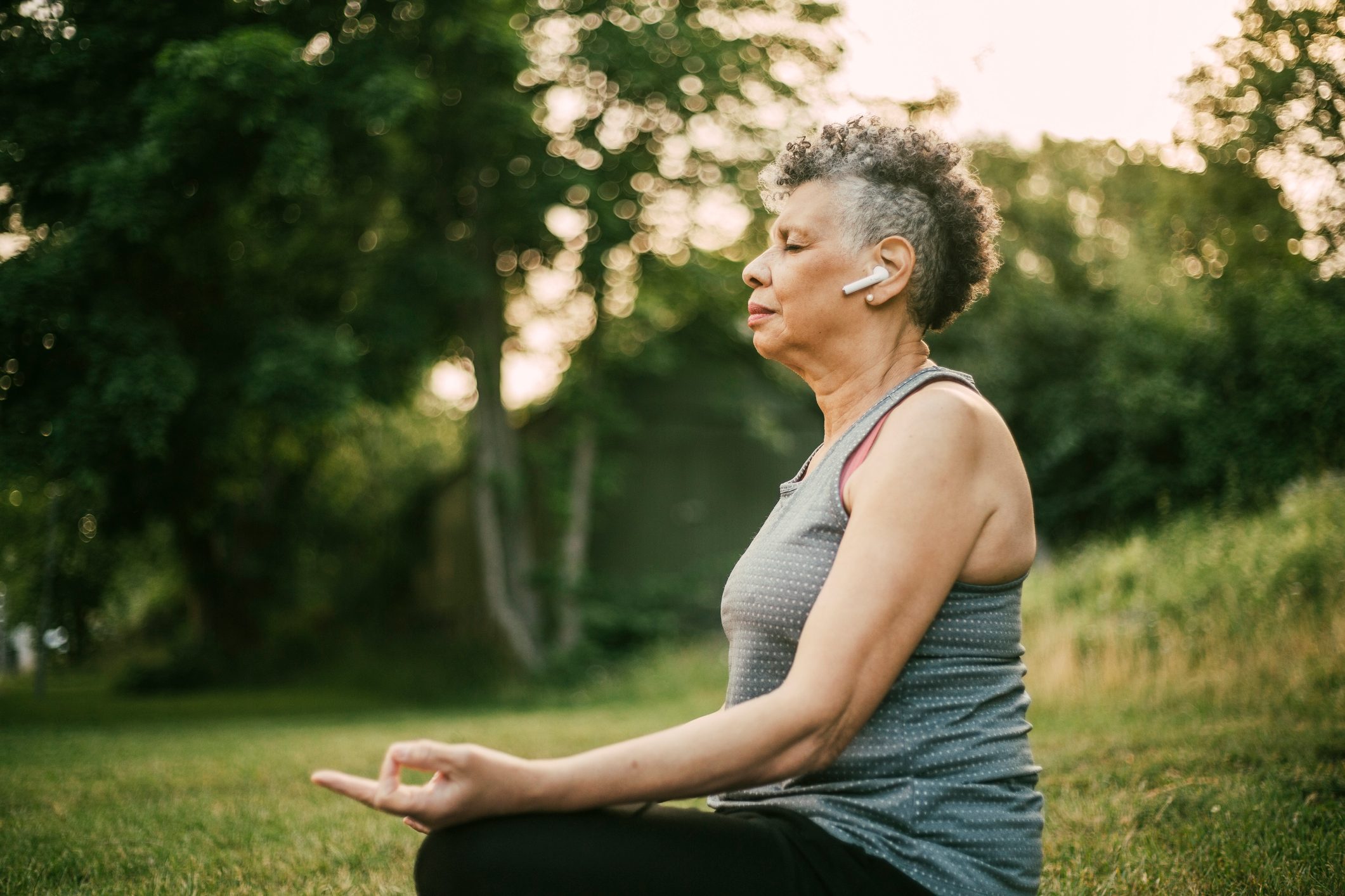 Side view of senior woman with in-ear headphones sitting in lotus position at park