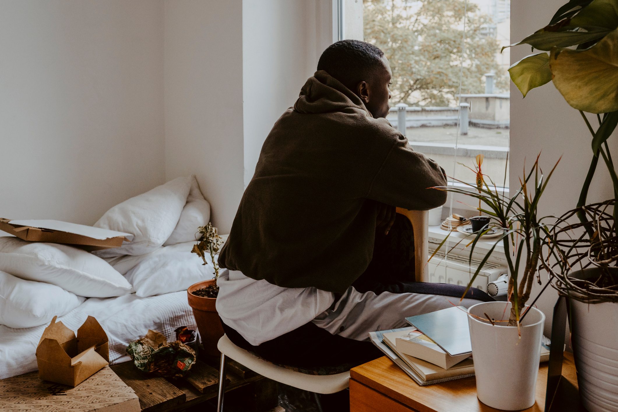 Rear view man looking through window while sitting in bedroom