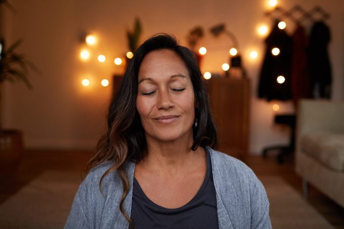 Serene mature woman smiling while meditating at home