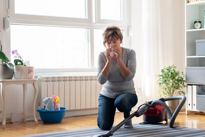 Senior woman cleaning carpet with a vacuum cleaner at home