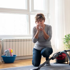 Senior woman cleaning carpet with a vacuum cleaner at home