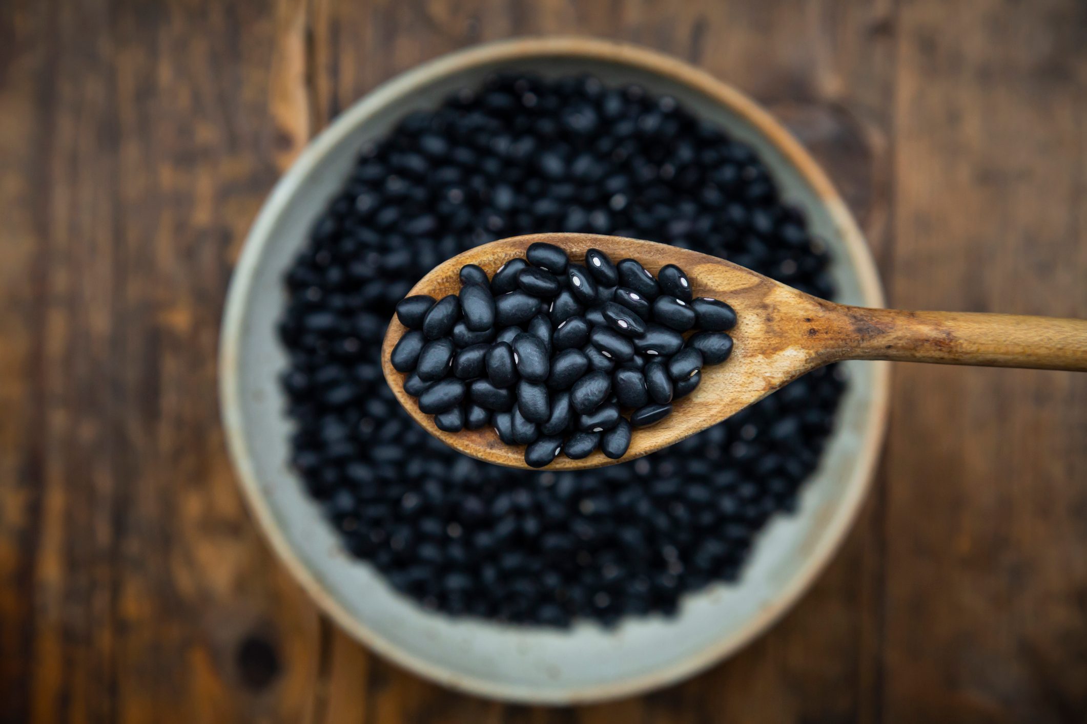 Overhead view of spoon and bowl of black bean on wooden table