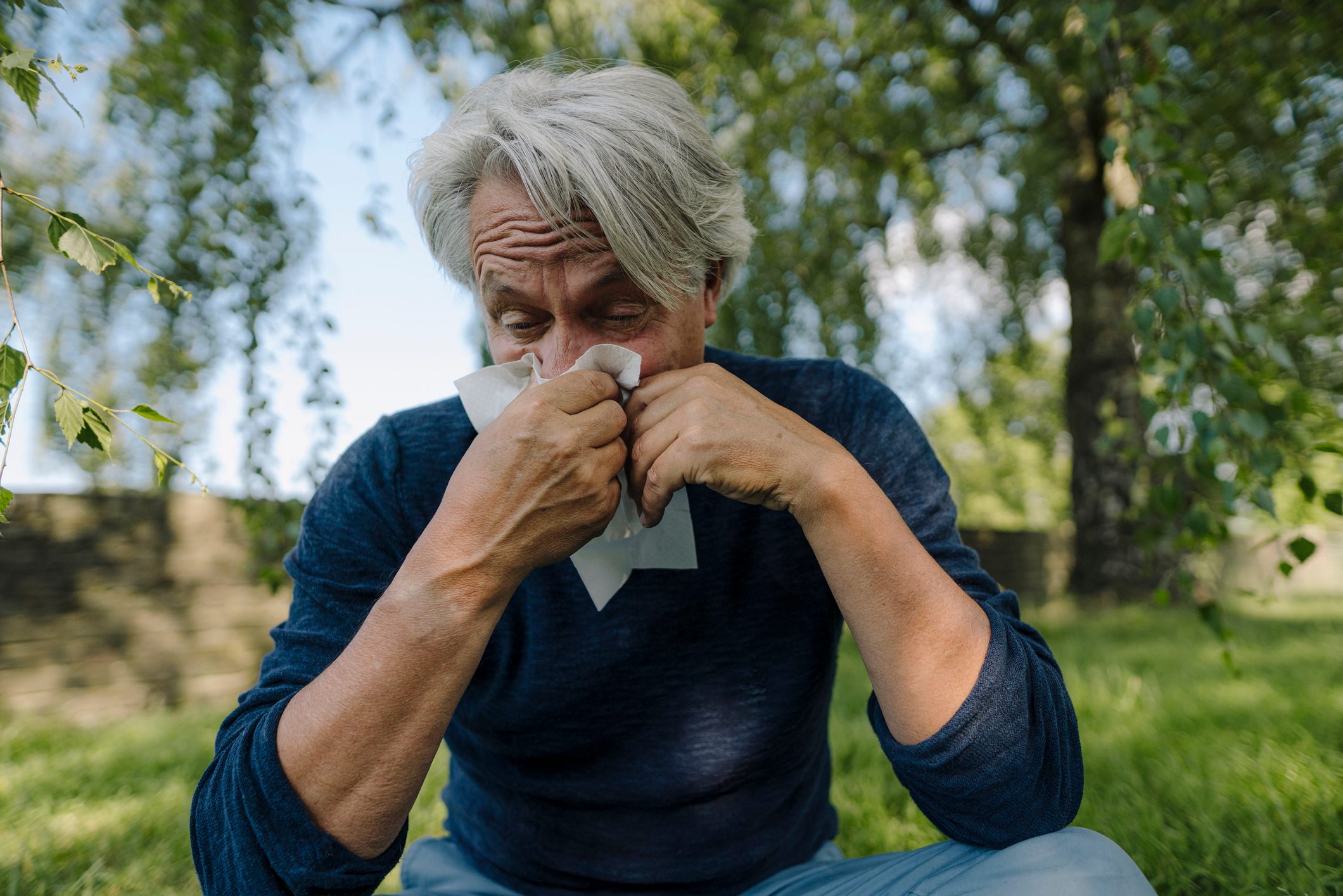 man blowing nose while sitting in field