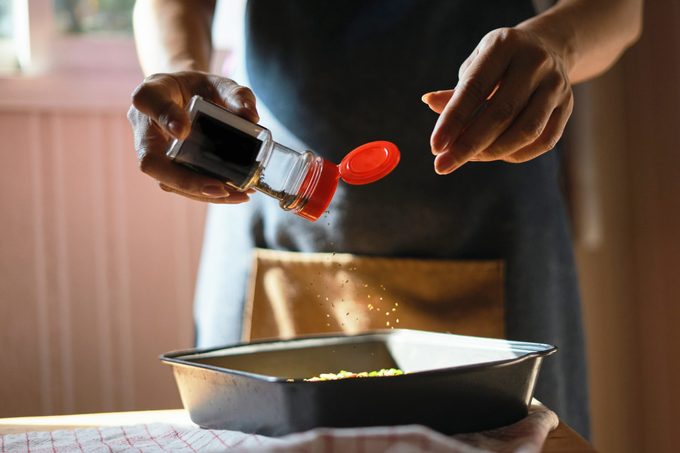 close up of woman adding seasoning to food while cooking