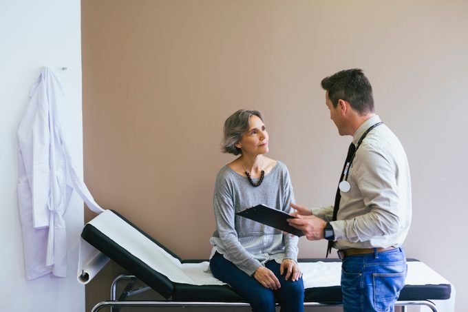 Senior patient talking with doctor while sitting on bed against wall at hospital