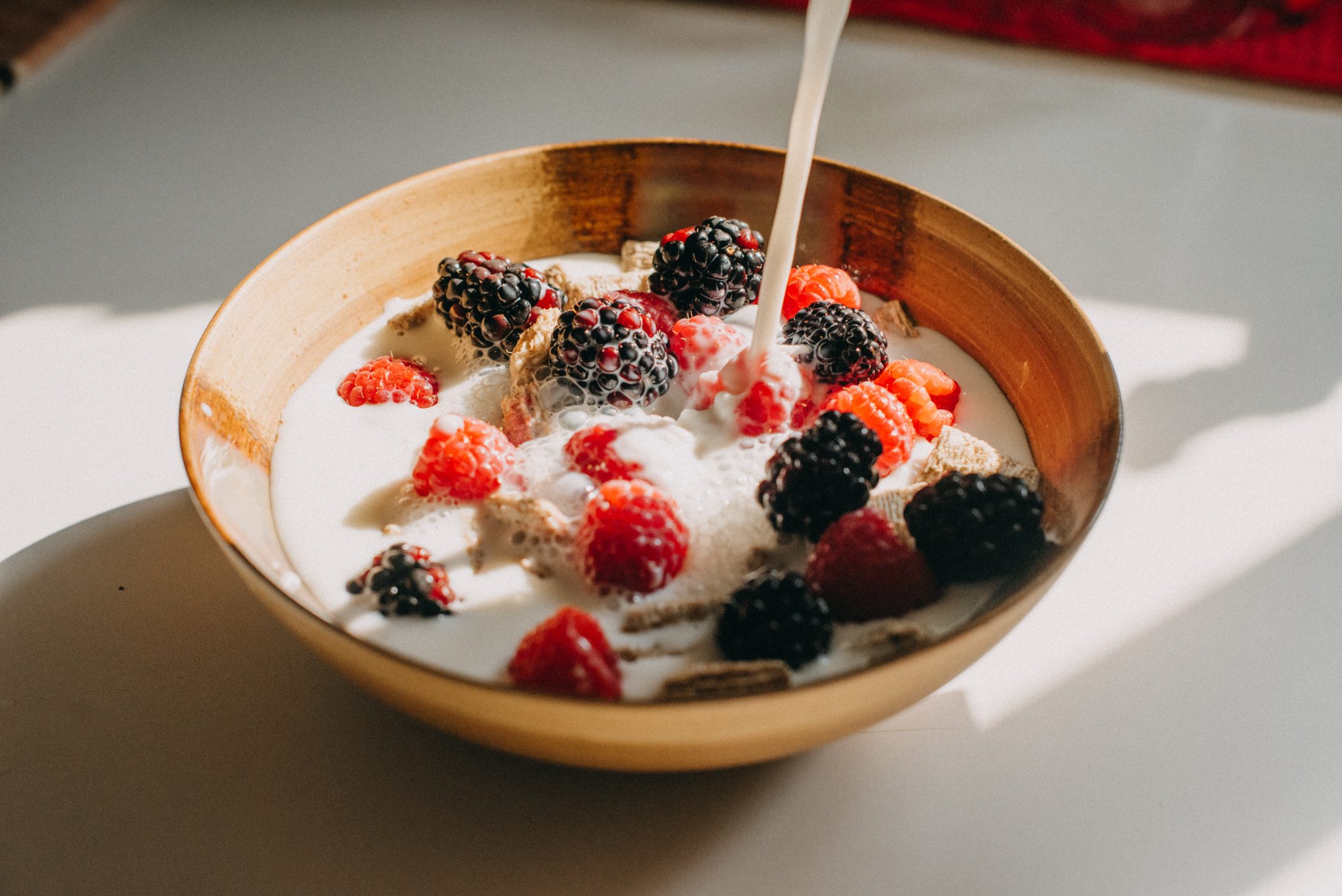 coconut milk being poured onto fruit cereal