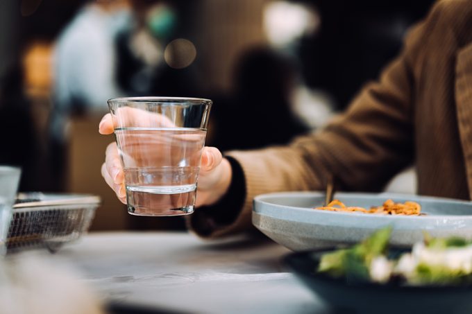 Close up of young woman drinking a glass of water while having meal in a restaurant.
