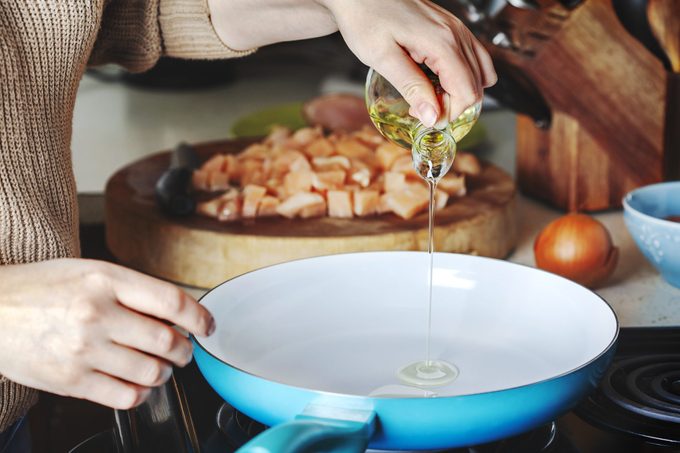 Woman pouring olive oil into skillet in kitchen while cooking