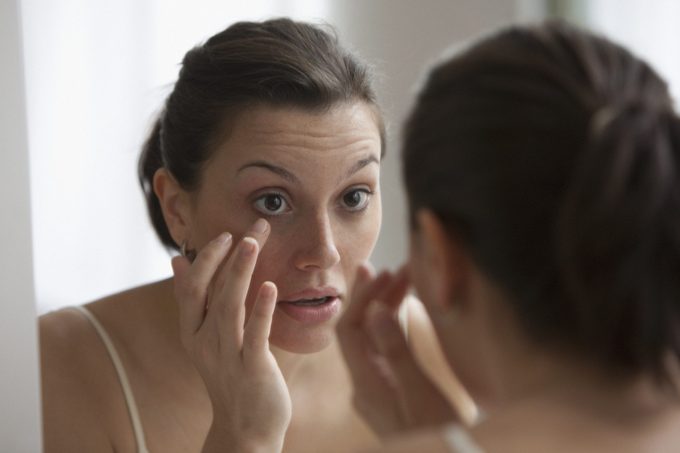 Young woman checking her eye in the mirror