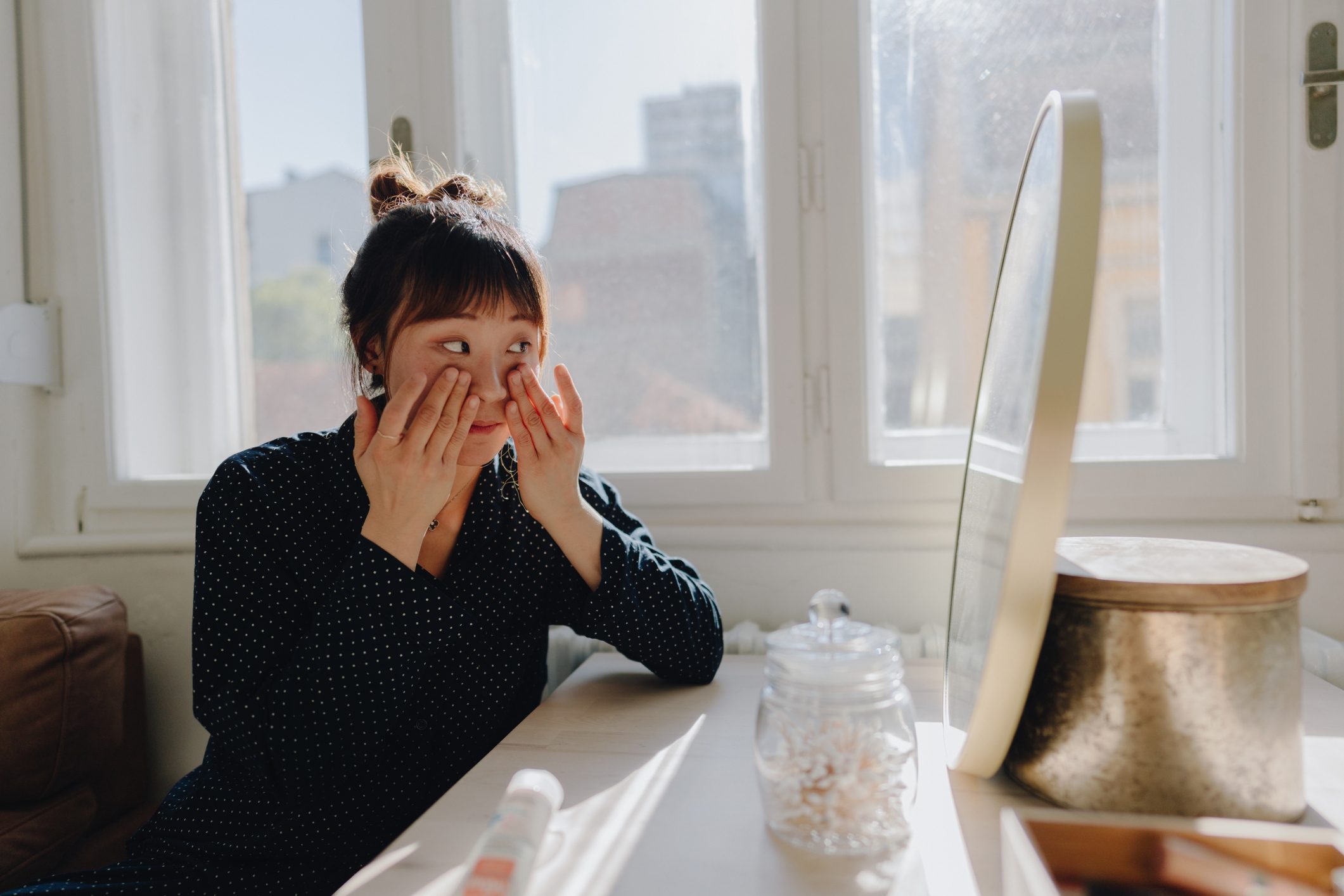 young woman doing skincare routine at home and applying eye cream to face