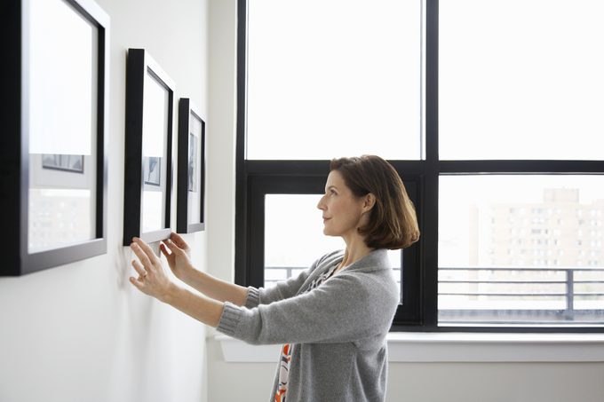 Woman Adjusting Picture Frame At Home