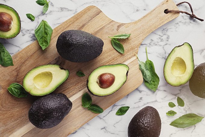 Wooden table with avocados and basil on marble stone