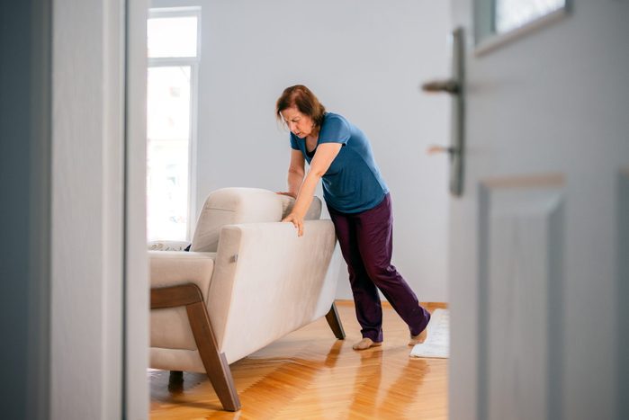 Woman suffering from dizziness with difficulty standing up while leaning on sofa
