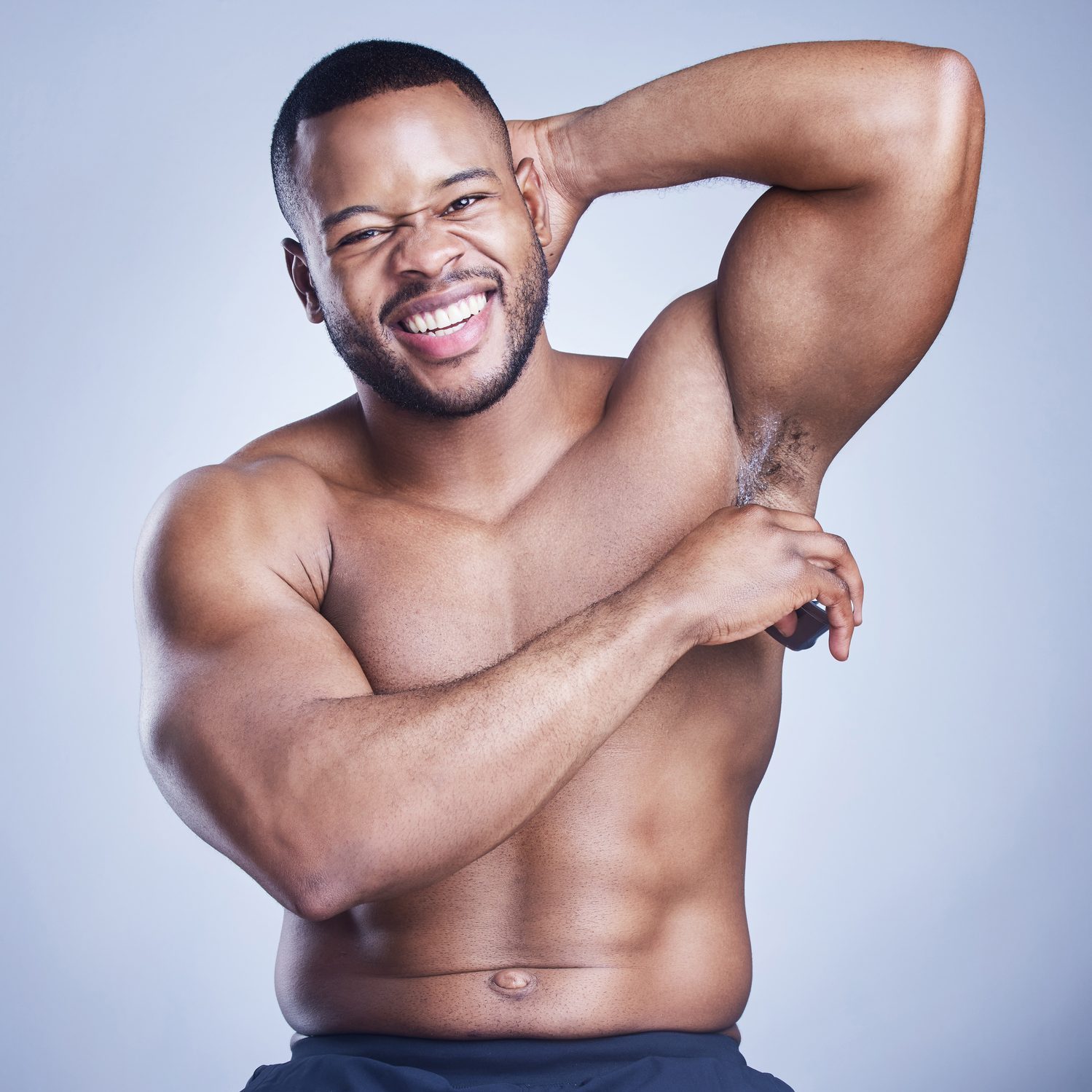 Studio shot of a handsome young man applying deodorant against a blue background