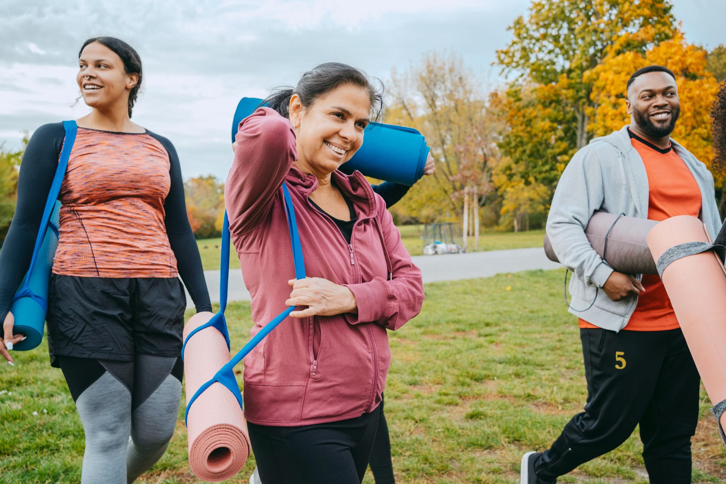 three people walking outside with yoga mats for bone strengthening yoga